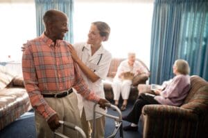 Smiling senior man with walker looking at female caretaker against modern healthcare backdrop, illustrating assisted living trends.